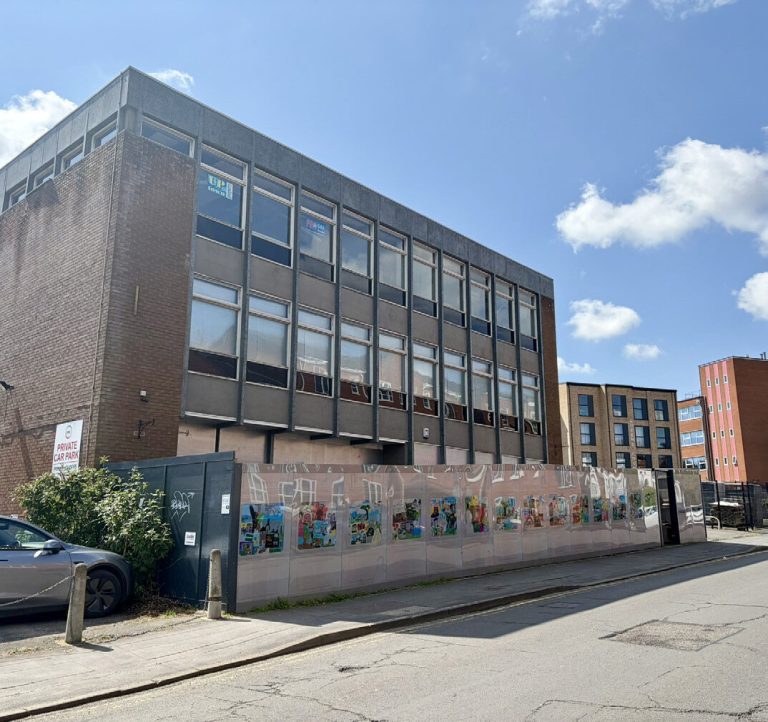 A vacant site on Albert Street behind a hoarding, next to a three-storey 1970s office block.