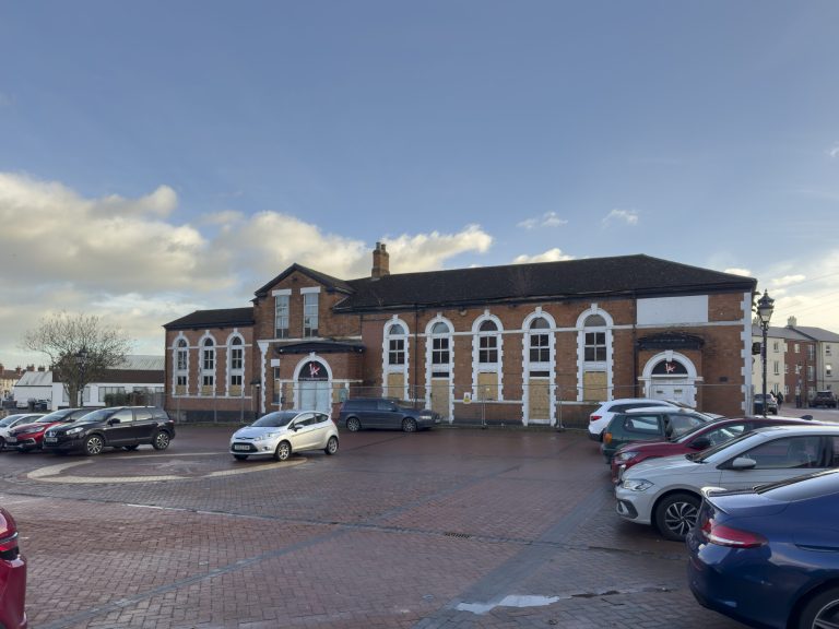 Brotherhood House, a long brick building with arched windows, beside a surface car park.