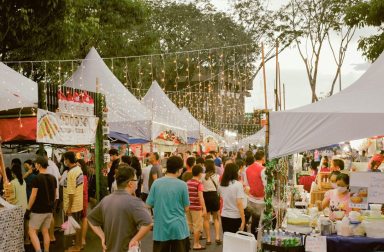 A busy outdoor market with white gazebos and crowds of people.