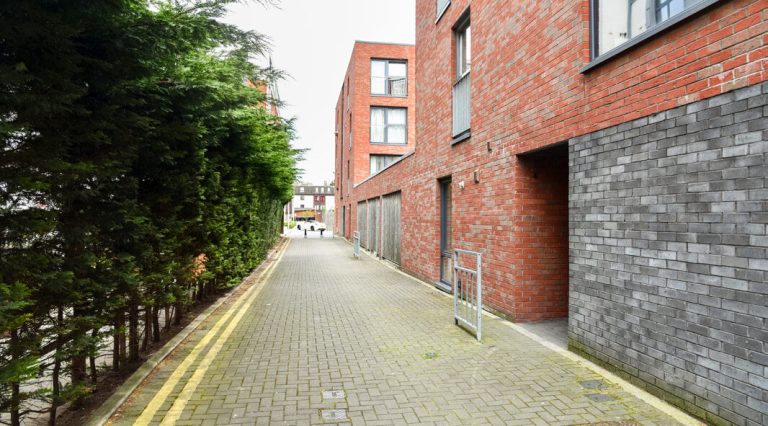 A paved walkway between a brick building and a row of trees.
