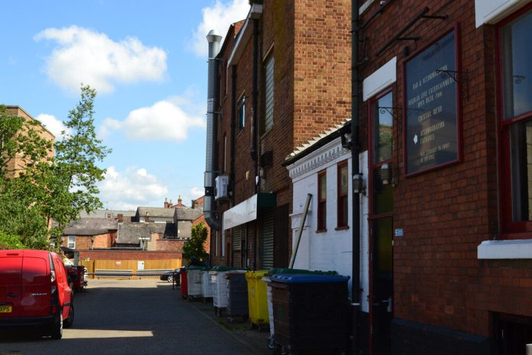 Drury Lane, a narrow street with the backs of brick buildings and parked cars.
