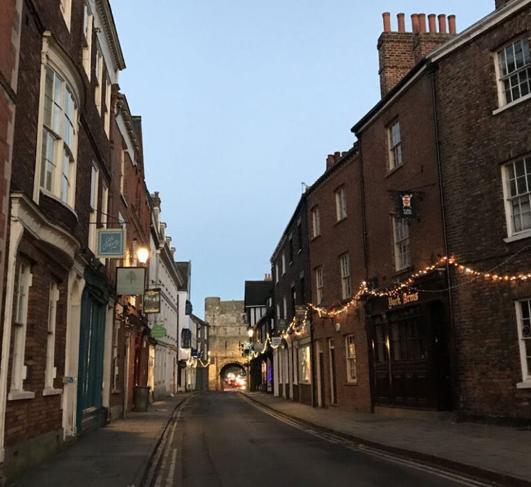 A historic street of brick buildings with festoon lights at dusk.