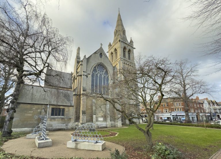 St Andrew's Church from the churchyard, with its tall spire and a modern sculpture in the foreground.