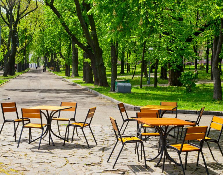 Café tables and chairs under the trees in a leafy public garden.