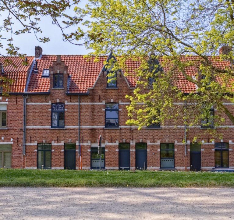 A terrace of red-brick homes with Dutch gables behind trees and a lawn.
