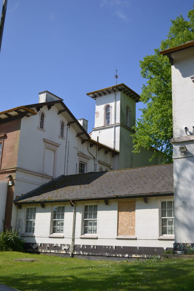 A white-painted listed building with a small clock cupola, among trees on the Town Hall site.