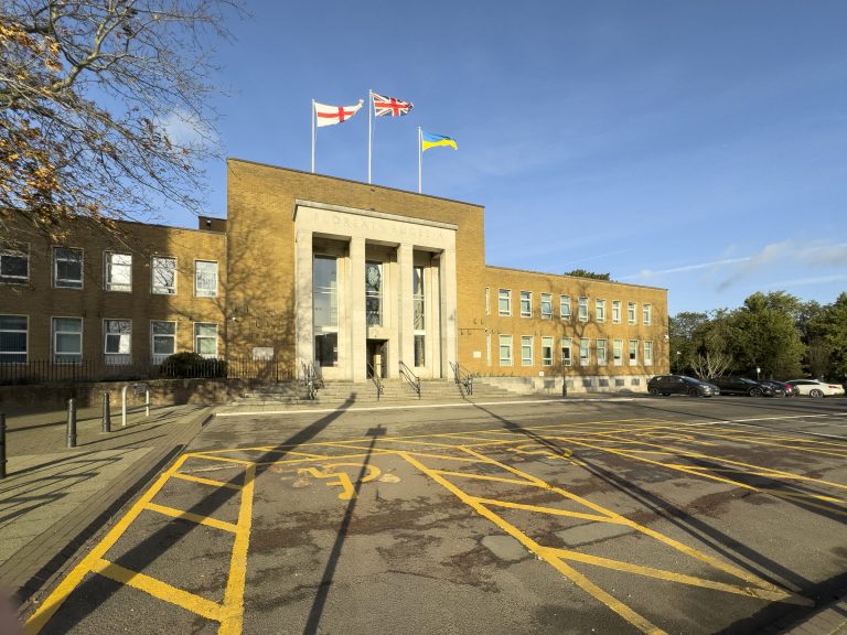 The front of Rugby Town Hall, a pale brick building with a tall columned entrance, behind a car park.