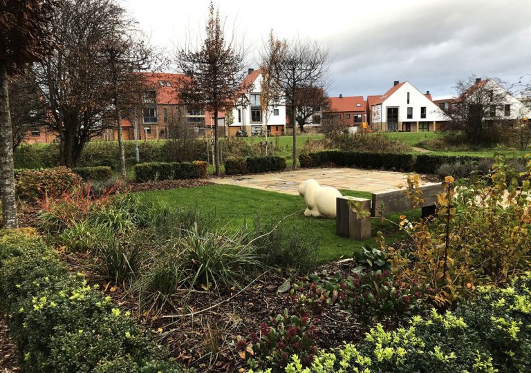 A landscaped garden with a sandpit and planting in front of new houses.